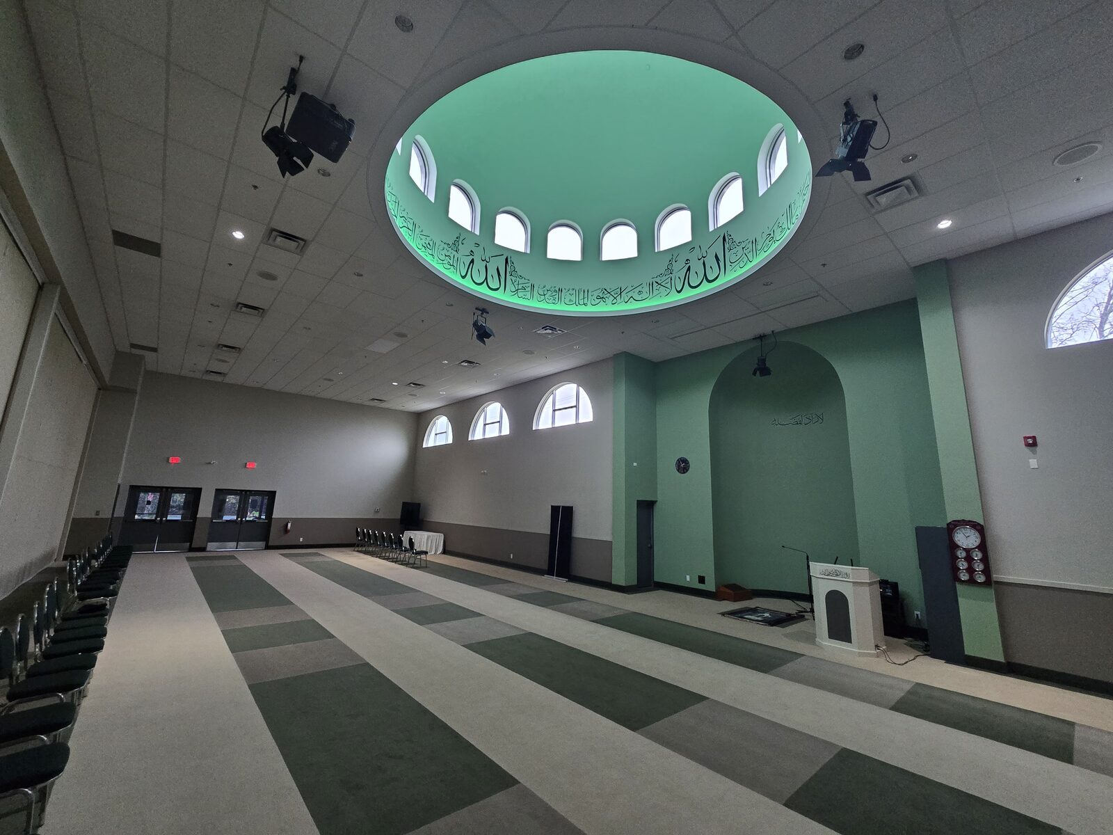 The main prayer hall dome, lit green, with Arabic calligraphy along its base